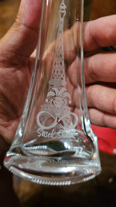 a vase that is eye shaped at the bottom and tapers. on one side is an image of the Eiffel Tower and the word bonjour. on the other side is t